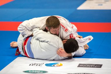 ABU DHABI, UAE - 19 Nisan 2016: ABU DHABI World PROFESSIAL JIU-JITSU CHAMPIONSIP 2016, IPIC ARENA. Beyaz kimonolu ve mavi kemerli dövüşçüler parterre içinde dövüşüyor..