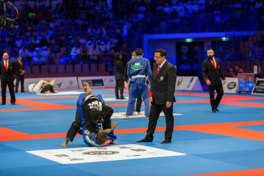 ABU DHABI, UAE - 19 Nisan 2016: ABU DHABI World PROFESSIAL JIU-JITSU CHAMPIONSIP 2016, IPIC ARENA. Mavi ve siyah kimonolu adamlar parterde savaşırken hakemler kurallara uyar..