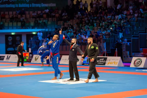 ABU DHABI, UAE - 19 Nisan 2016: ABU DHABI World PROFESSIAL JIU-JITSU CHAMPIONSIP 2016, IPIC ARENA. Siyah-mavi kimonolu dövüşçüler. Hakem kazananı ilan ediyor..