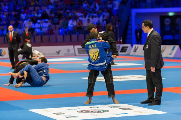 ABU DHABI, UAE - 19 Nisan 2016: ABU DHABI World PROFESSIAL JIU-JITSU CHAMPIONSIP 2016, IPIC ARENA. Mavi ve siyah kimonolu dövüşçüler kavga ediyor. Yanlarında hakem var..