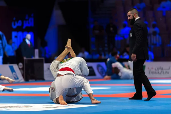 ABU DHABI, UAE - 19 Nisan 2016: ABU DHABI World PROFESSIAL JIU-JITSU CHAMPIONSIP 2016, IPIC ARENA. Beyaz kimonolu adamlar parterde kavga ediyorlar. Hakem yakınlarda..