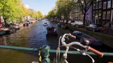 Amsterdam 'daki kanalı bisikletle seyredeceğiz. Kanalda yelken açan bir tekne.