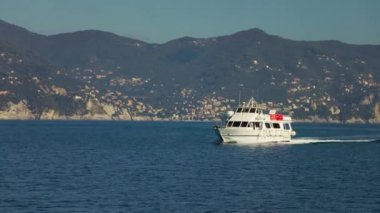 Arka planda dağlar boyunca denizde çamurlukları olan bir tur teknesi. Burası Liguria, İtalya..
