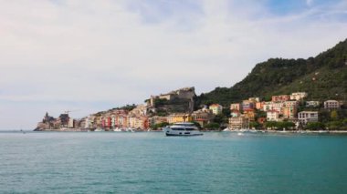 İtalya, Liguria 'da Porto Venere yakınlarında demirli beyaz bir yat. Kasabada renkli binalar görüyoruz..