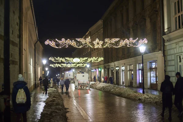 In the downtown of Krakow people and white carriage with horses rides at night.