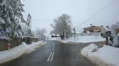 POV Point of view of car drives along the road in winter village with people and cars in snowy Poland.