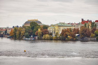 Prague cityscape view of Vltava and buildings in autumn with colorful trees.