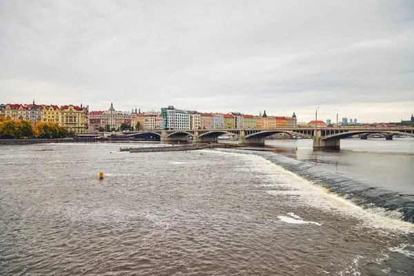Wide view of Jirasek Bridge, colorful historical buildings and Dancing House in Prague.