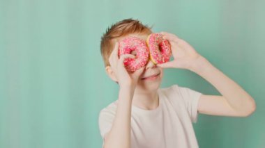 Boy in t-shirt with donuts as an eyes smiling in a National doughnut day. Slow motion video.