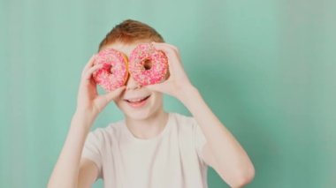 Ulusal çörek gününde donutları bol bol gülümseyen beyaz tişörtlü bir çocuk. Yavaş çekim videosu.