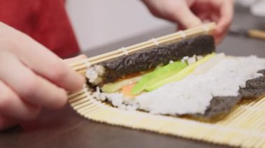 Boy rolls sushi with bamboo mat. Slow motion video.