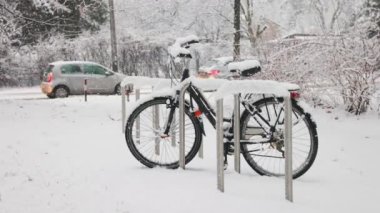 Black bicycle under falling snow next to road with moving cars in Krakow, Poland. Slow motion video.
