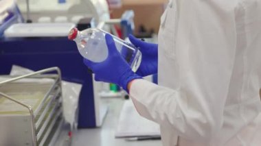 Laboratory assistant writes on a bottle with clear liquid before researching.