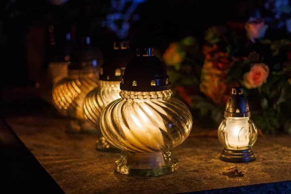 stock image Grave lanterns with burning candles on stone surface at night.