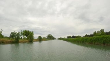 Tekne alçak kıyıları olan bir kanal boyunca yelken açar. Bulutlu gökyüzü ve yeşil çimenler.