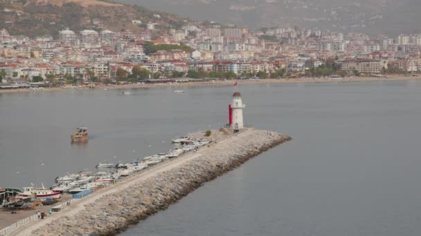 トルコのアランヤの水と風光明媚な景色に沿って散歩するための絵のような設定の小さな灯台 ライトハウスは市民の港の上に立っています 白い塔の上からのトルコの旗の波 — ストック動画
