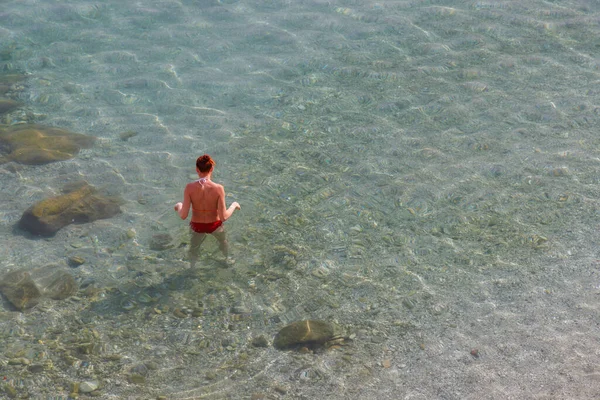 Sakin denizde beline kadar duran bir kadın. Kırmızı bir mayo giyiyor..