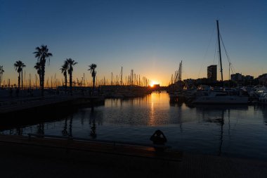 Alicante, İspanya 'da yat marinasında gün batımı. Bankta oturan adam.