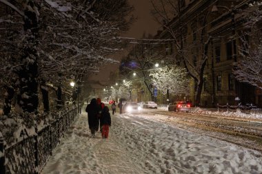 İnsanlar Krakow yolu boyunca karlı bir gece caddesi boyunca yürürler. Yolda trafik vardı..
