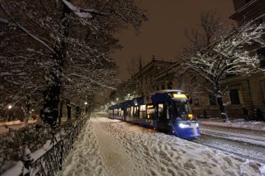 Mavi, modern bir tramvay gece Krakow 'da karlı bir cadde boyunca yol alır..