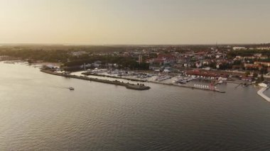 Polonya 'nın Gizycko kentinden gün batımında gölün üzerinden çarpıcı bir hava manzarası. Altın gökyüzü, sakin su ve şehrin ufuk çizgisi huzurlu ve resim gibi bir manzara yaratır..