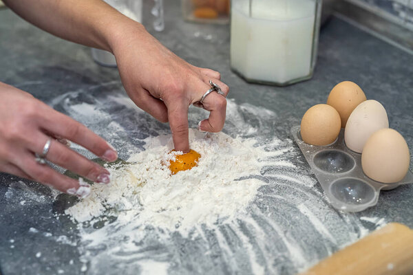 breaking eggs with women's hands into flour to make dough for cakes. The concept of cooking on the desktop