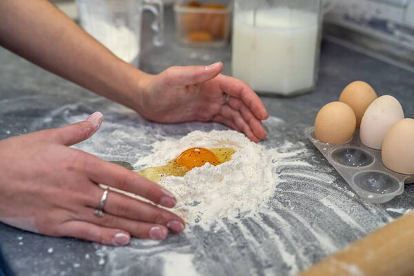at a large spacious table a woman prepares dinner where she breaks eggs and kneads dough for casserole. Cooking concept