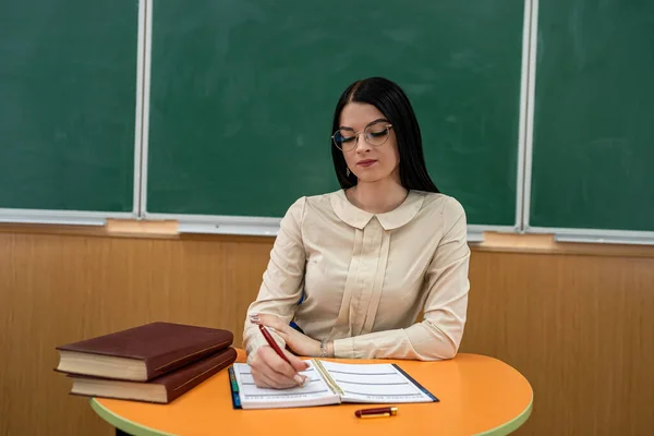 Woman teacher sits at a table with books and notebooks, studying concept