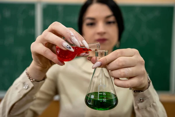 Chemistry female teacher observing reaction test-tube at classroom and against green blackboard. Experimentation