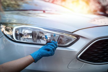 Eldivenli el, güzel bir arabanın farlarının yanında bir gelagon lambasını tutuyor. Araba tamiri konsepti. Farlar için lamba konsepti