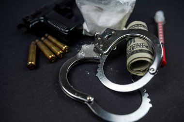 Susturuculu uyuşturucu ve para tabancası ve siyah masada izole edilmiş kelepçe. Uyuşturucu satmak. Uluslararası suç. Yasadışı uyuşturucu madde dolaşımının kontrolü.