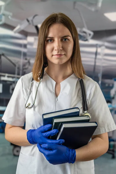 young beautiful doctor woman standing in the operating room with books in her hands. medicine. doctor with books