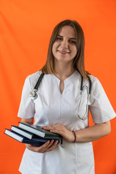 Smiling female doctor with stethoscope and books in hands posing isolated on plain background. Woman doctor concept. Portrait of a woman