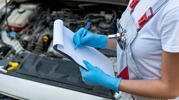 female mechanic stands with a tablet with a list of breakdowns to the chassis of a car in a workshop in a car repair center. car. female engineer inspecting car parts