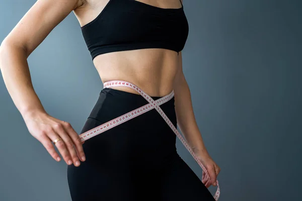 Sporty fit woman measuring with tape measure and measuring waist after dieting isolated over gray background. Dietetics. Weight loss fitness. size measurement
