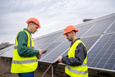 Tulum giymiş işçiler güneş panellerini incelemeye geldiler. Yeşil elektrik kavramı