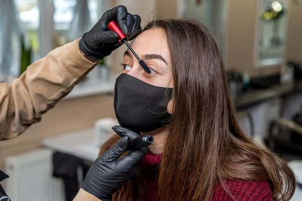a beautiful young client in a special black mask came to the salon for makeup during a pandemic. The concept of beauty services during a pandemic