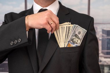 Şık ceketli yakışıklı ve genç bir iş adamı. Hem de bol paralı bir takım elbiseden. Büyük ve küçük işletme konsepti. Dolarlar bir adamın ellerinde.