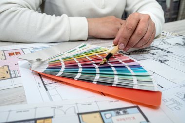 view of a man working on the design of the apartment according to the finished drawing. Man's hands on the table. Drawings and palettes with colors.