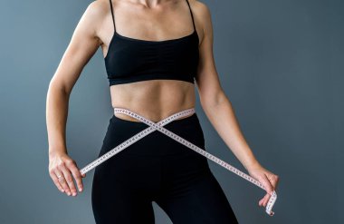 Gri arka planda izole edilmiş diyet sonrası ölçü ve bel ölçüsü alan sportif formda bir kadın. Diyetikler. Kilo verme kondisyonu. boyut ölçümü