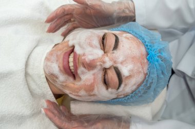 Koruyucu eldivenli kadın kozmetik uzmanı bir müşterisiyle kuaförde çalışıyor. Yüz güzelliği için maske takıyorum. Yüz temizleme