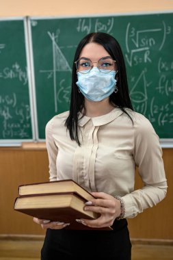 Coronavirus salgını sırasında tahtaya karşı duran tıbbi maskeli bir öğretmenin portresi. Eğitici matematik dersi.