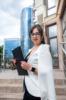 Portrait of a business woman with chic hair and great makeup standing near a high-rise building. Business style concept. A woman who works in the office