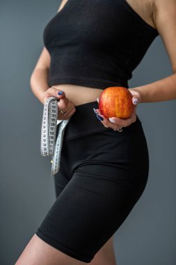 Spor kıyafeti giyen spor eğitmeni kadın, gri arka planda izole edilmiş elma ölçme bandı tutuyor. Spor konsepti. sağlıklı vücut durumu