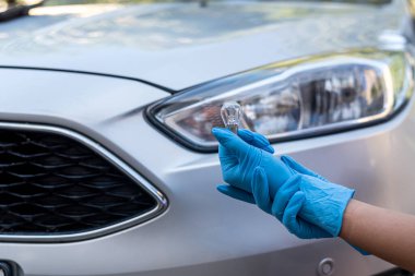 Çalışkan elleri olan tamirci arabanın farının yanında bir halojen ampul tutuyor. Bir tamirci tarafından araba tamiri. Bir halojen lamba değiştirmek