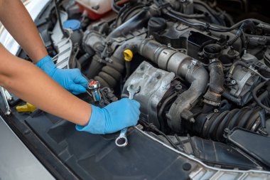 Araba tamirhanesinde, gülümseyen genç bir kadın tamircinin ellerini kapatıyorlar. Kadın tamirci. Kadın elleri kaputun altında.