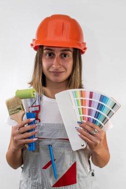 Yüzünde mutlu bir ifadeyle kameraya bakan kasketli kadın inşaat işçisi. Kadın tulum ve koruyucu bir kask giymiş. tipik bir arkaplanda izole edilmiş.