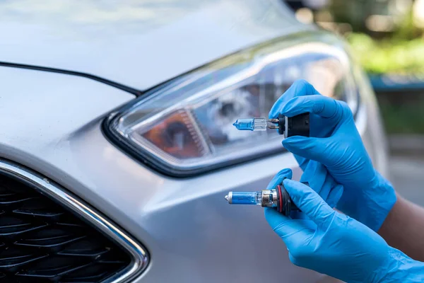 stock image Hands of strong man mechanic hold halogen car lamps against headlights and repair car. car repair by a strong mechanic. lamp in hand