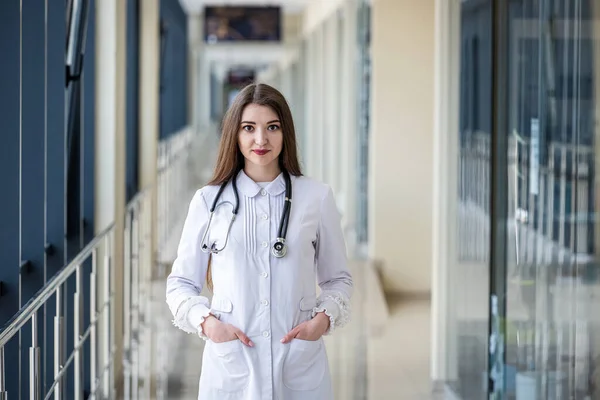 stock image A beautiful young doctor is standing in the hospital corridor with a stethoscope around her neck. Concept of medicine. Doctor with a stethoscope