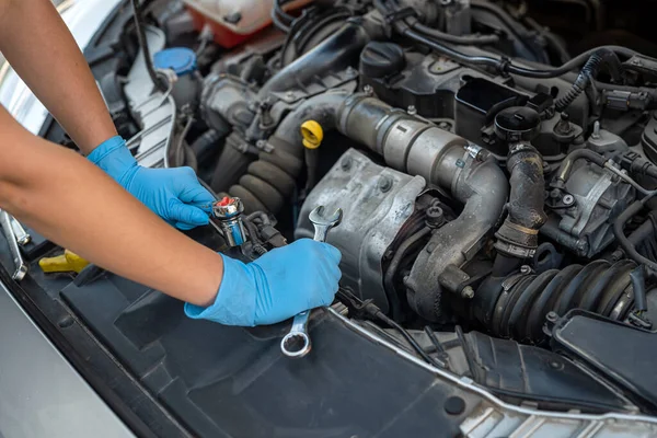 Araba tamirhanesinde, gülümseyen genç bir kadın tamircinin ellerini kapatıyorlar. Kadın tamirci. Kadın elleri kaputun altında.